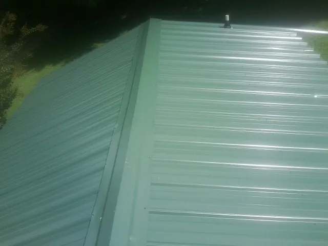 New green metal panels meeting at the ridge of a roof — Flat Roof Repair work by our crew in Frenchtown