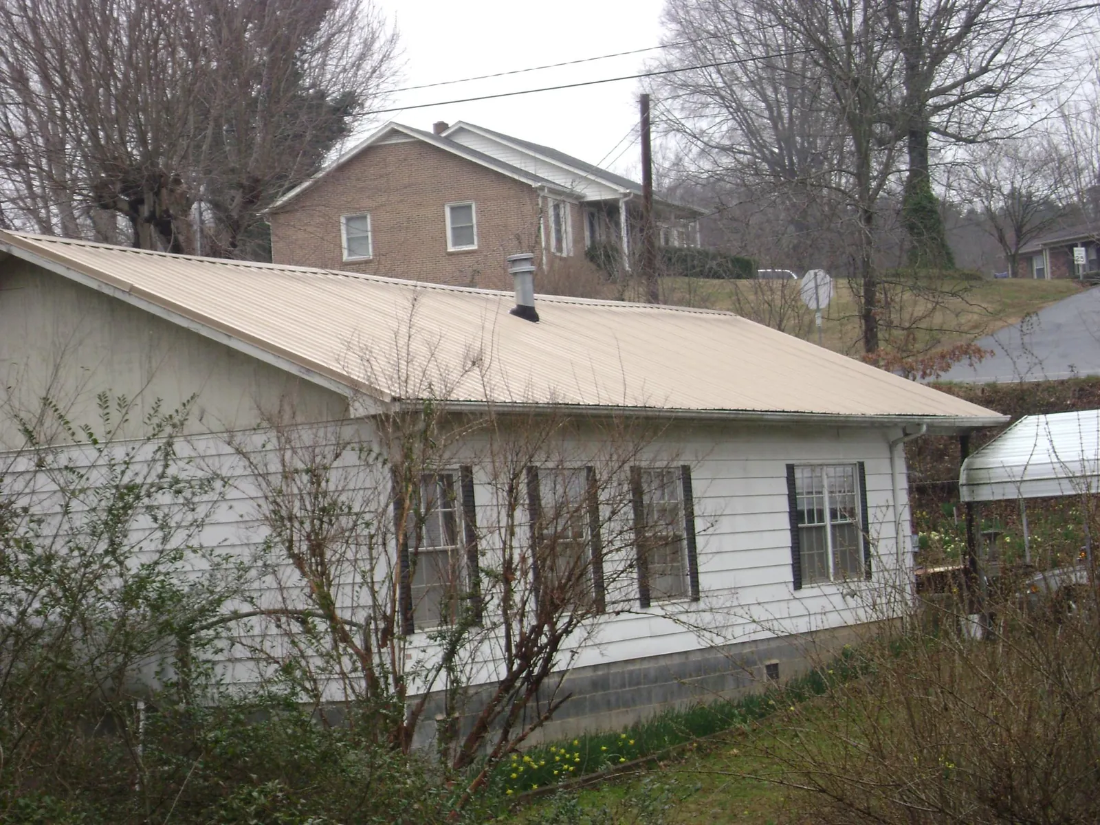 Tan metal roof on a white sided house set into a hillside — Commercial Roofing by Roofing Brothers in Frenchtown